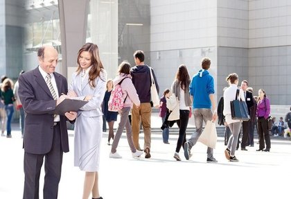 公共の場でスーツを着て資料を見ながら会話する男女画像